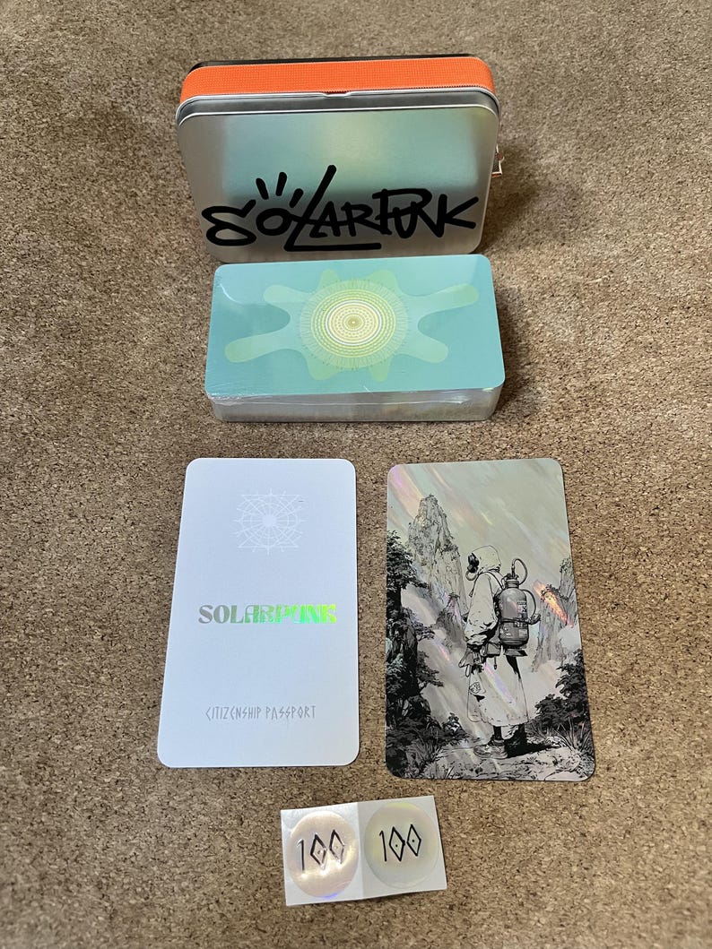 May include: A silver metal tin with an orange lid and the text SOLARFUN, a deck of cards with a light blue abstract design, a white card labeled SOLARFUN CITIZENSHIP PASSPORT, a holographic card featuring a figure in a landscape, and two circular 100 stickers.