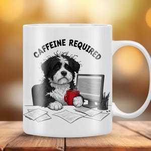 Puede incluir: Taza de cerámica blanca con una ilustración de un perro en blanco y negro y el texto "CAFFEINE REQUIRED". El perro está en un escritorio con una computadora, una taza roja y papeles. La taza tiene un asa blanca.