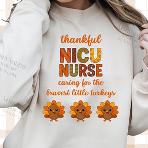 May include: Cream-colored sweatshirt with the text "thankful NICU NURSE caring for the bravest little turkeys" in orange and brown. Features three cartoon turkeys with orange and yellow feathers.