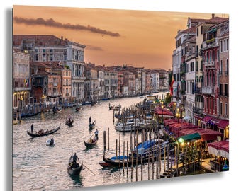 May include: A scenic canvas print of Venice, Italy, featuring gondolas on a canal at sunset. Buildings line the waterway, with warm hues of orange and red in the sky. The image captures the romantic atmosphere of the city.