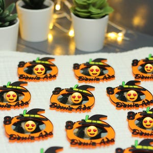 Könnte beinhalten: Eine Sammlung orangefarbener Kürbisdekorationen mit schwarzen Hexenhüten und dem Text "Deniz Ada". Jeder Kürbis hat ein Herzaugen-Emoji. Die Dekorationen sind wahrscheinlich für Halloween oder den Herbst.