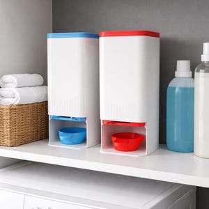 May include: Two white laundry detergent dispensers with coloured lids and matching bowls. One has a blue lid and bowl, the other has a red lid and bowl. The dispensers sit on a shelf above a washing machine, with laundry supplies nearby.