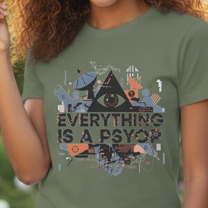 May include: Olive green t-shirt featuring a graphic design with a triangle, an eye, and the text "EVERYTHING IS A PSYOP." The design includes various abstract shapes and lines in shades of blue, orange, and gray.