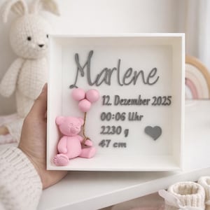 Peut inclure: Boîte blanche avec le nom "Marlene" en script gris. Un ours en peluche rose tient trois ballons roses. La boîte comprend la date, l'heure, le poids (2230 g) et la taille (47 cm).