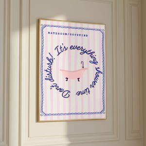 May include: A framed bathroom art print with a pink and white striped background. The print features a pink bathtub illustration and the text "Don't disturb! It's everything shower time" in a circular design. The words "Bathroom/Occupied" are at the top.