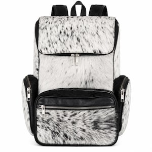 May include: A backpack featuring a white and black speckled animal hair texture on the main body and front pocket. The bag includes black leather trim, silver-tone metal zippers on the front and side compartments, and black shoulder straps.