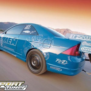 May include: A blue sports car with a large rear wing and custom graphics. The car has black wheels and various sponsor logos, including "AEM" and "Import Tuner". The background shows a desert landscape.