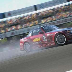 May include: A red sports car with black accents drifts on a racetrack, kicking up a cloud of smoke. The car has the number 04 on the side and sponsor logos. A grandstand with spectators is visible in the background.