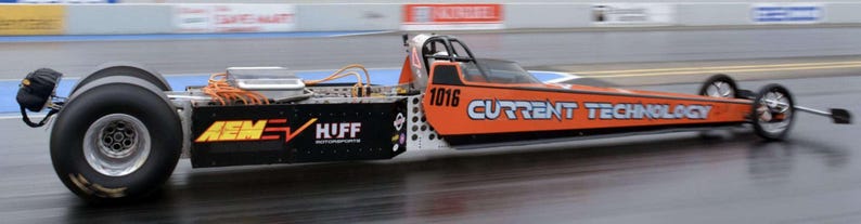 May include: An orange and black dragster with the text "CURRENT TECHNOLOGY" and the number "1016" on the side. The dragster has large rear tires and small front tires. The vehicle is on a racetrack.