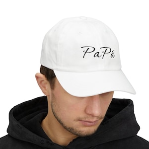 May include: White baseball cap with the word "Papá" in black script. The cap is made of a soft material and has a curved brim. The hat is a classic style, suitable for everyday wear.