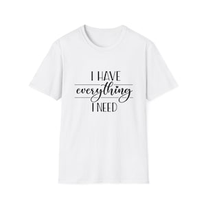 Könnte beinhalten: Weißes T-Shirt mit dem schwarzen Text "I HAVE everything I NEED". Der Text ist in einer Mischung aus Block- und Schreibschrift gehalten. Das T-Shirt hat einen Rundhalsausschnitt und kurze Ärmel. Der Text ist zentriert.
