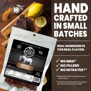 K&ouml;nnte beinhalten: Eine Packung Boston Brisket Works Buffalo Exotic Jerky mit einer B&uuml;ffel-Illustration vor einem Holzbrett mit Jerky, Zitronenscheiben und Gew&uuml;rzen. Die Packung weist "Hand Crafted in Small Batches" und "No MSG, Fillers, or Nitrates" auf.