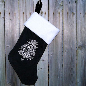 May include: Black Christmas stocking with a white cuff and a white embroidered design of a woman's profile in an ornate frame.