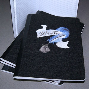 May include: A stack of black notebooks with a white and blue embroidered design of a quill pen and inkwell. The design includes the word "Write".