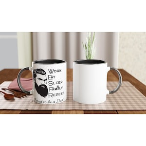 May include: White ceramic mug with a black interior and silver handle. The mug features a black and white illustration of a bearded man and the words "WORK, EAT, SLEEP, FAMILY, REPEAT" and "Proud to be a Dad".
