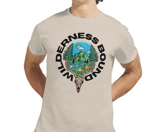 以下が含まれることがあります： 「Wilderness Bound」と書かれた円形グラフィックのベージュTシャツ。グラフィックは、木、川、テント、鹿の頭蓋骨のある山のシーンを特徴としています。Tシャツは半袖です。