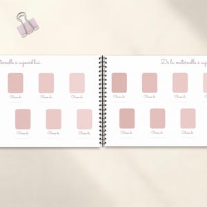 May include: A spiral-bound journal with a light pink cover and pages. The journal is open, displaying two facing pages with a series of pink rectangular boxes. The text "De la maternelle &agrave; aujourd'hui" is written at the top of each page. A light pink binder clip is at the top.