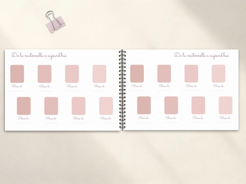 May include: A spiral-bound journal with a light pink cover and pages. The journal is open, displaying two facing pages with a series of pink rectangular boxes. The text "De la maternelle &agrave; aujourd'hui" is written at the top of each page. A light pink binder clip is at the top.
