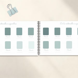May include: Open notebook with a spiral binding, featuring a series of rectangular color swatches in shades of teal and blue-green. The text "De la maternelle &agrave; aujourd'hui" is written at the top of each page. A light blue binder clip rests above the notebook.