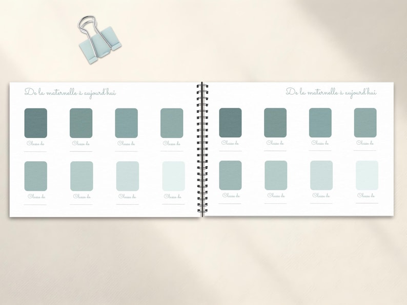 May include: Open notebook with a spiral binding, featuring a series of rectangular color swatches in shades of teal and blue-green. The text "De la maternelle &agrave; aujourd'hui" is written at the top of each page. A light blue binder clip rests above the notebook.