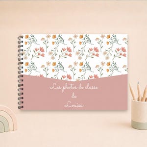Peut inclure: Un carnet à spirales avec une couverture blanche ornée d'un motif répétitif de petites fleurs orange et roses sur des tiges vertes. La partie inférieure est d'un rose poudré uni avec le texte blanc Les photos de classe de Louisa.
