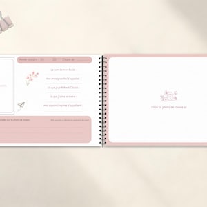 May include: Open spiral-bound memory book with pink accents. The left page has space for a photo and prompts. The right page has a camera graphic and space for a class photo. A paper clip rests above the book.