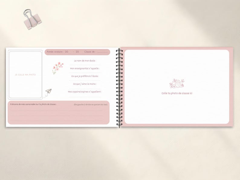 May include: Open spiral-bound memory book with pink accents. The left page has space for a photo and prompts. The right page has a camera graphic and space for a class photo. A paper clip rests above the book.