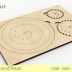 Könnte beinhalten: Eine lasergeschnittene Holzplatte mit kreisförmigen Zahnraddesigns und dem Text "EsTetiKoArt" und "LASER CUT DIGITAL FILES". Die Platte hat eine hellbraune Farbe mit dunkelbraunen Kanten. Das Design umfasst drei kreisförmige Zahnräder.