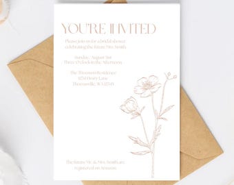May include: A white invitation card with the text "YOU'RE INVITED" in a rose gold font. The card includes event details and a floral illustration. It rests on a brown envelope.