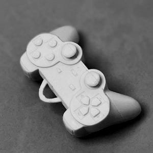 以下が含まれることがあります： 白のプラスチック製ゲームコントローラー。十字キー、アクションボタン、ショルダーボタンを備えたクラシックなデザイン。画像はモノクロで、コントローラーに焦点を当てています。
