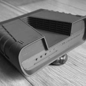 May include: A dark gray, rectangular object with a ridged top and rounded edges. The object has a series of small, circular indentations along one side. It appears to be resting on a small, rounded base. The object is likely a piece of technology or a component.