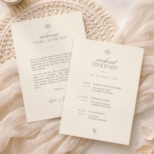 Könnte beinhalten: Zwei cremefarbene Papierkarten mit dunkelgrauem Text. Eine Karte ist mit welcome FAMILY & FRIENDS betitelt, die andere mit weekend ITINERARY für den 31. Juli bis 2. August 2025. Beide Karten zeigen ein kleines Muschelsymbol und eine elegante Serifenschrift.
