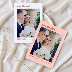以下が含まれることがあります： 笑顔のカップルの写真が写った、2枚の「save the date」カード。カードには赤い筆記体で「save the date」と書かれています。「Isabella & Oliver」という名前が写真の下に印刷されています。1枚は白、もう1枚はピーチ色です。