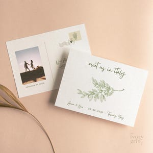 Puede incluir: Juego de invitación de boda de dos partes. La tarjeta frontal dice "meet us in Italy" con una ilustración de rama de olivo. La tarjeta trasera tiene una foto de una pareja y el texto "Invitation to follow". La fecha 26.06.2030 y la ubicación Toscana, Italia también están impresas.