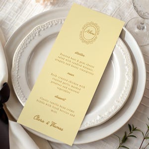 Może przedstawiać: Wysoka, jasnożółta, prostokątna karta menu z ozdobną owalną ramką wokół słowa Menu. Tekst zawiera listę przystawek, dań głównych i deserów, a na dole znajdują się imiona Clara & Thomas zapisane kursywą.