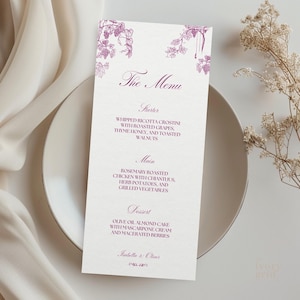 May include: A cream-coloured menu card featuring a purple grape vine design. The menu details a starter, main course, and dessert, including whipped ricotta crostini, rosemary roasted chicken, and olive oil almond cake. The text "The Menu" is at the top.