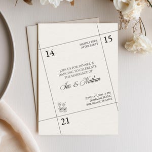 May include: A cream-colored wedding invitation card featuring black text and thin diagonal lines. The text reads: Join us for dinner & dancing to celebrate the marriage of Iris & Nathan, June 14th, 2030, 6 PM, Domaine Blanc, Bordeaux, France.