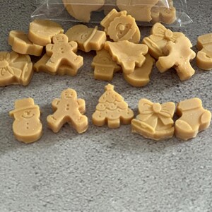 Puede incluir: Fundidos de cera navideños de color marrón claro, con formas de muñeco de nieve, hombre de jengibre, árbol de Navidad, lazo y calcetín. Algunos están en una bolsa transparente, otros sobre una superficie gris.