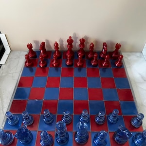 Könnte beinhalten: Ein komplettes Schachspiel mit rot-blauen Quadraten. Die Schachfiguren sind rot und blau, mit den roten Figuren auf der einen und den blauen Figuren auf der anderen Seite. Das Brett ist quadratisch.