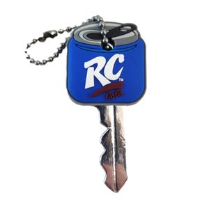 May include: A metal key with a blue rubberized head shaped like an RC Cola soda can. The head features the white RC Cola logo and a silver pull tab design. A silver-toned metal ball chain is attached to the top of the key head for hanging.