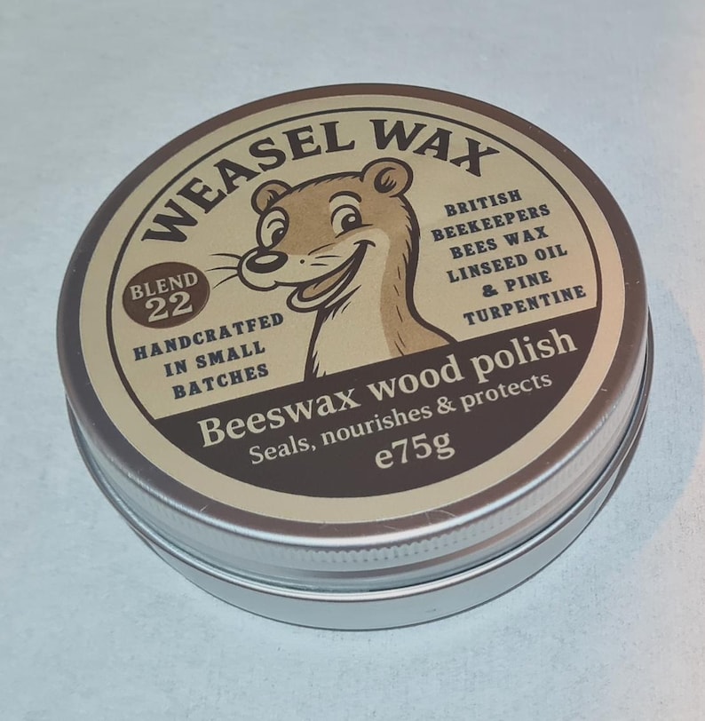 May include: A circular metal tin of Weasel Wax beeswax wood polish. The label features a cartoon weasel and text that reads "Blend 22" and "Handcrafted in small batches." The tin contains 75g of polish.