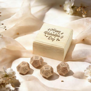 Può includere: Una scatola di legno con la scritta "Happy Valentine's Day" e quattro dadi dodecaedrici in legno. I dadi hanno illustrazioni e testo incisi. La scatola e i dadi sono su un tessuto color crema con fiori bianchi.