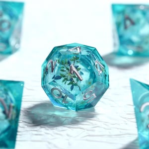 Peut inclure: Un ensemble de dés polyédriques avec un design transparent turquoise. Chaque dé présente une numérotation argentée et un motif floral encapsulé. Les dés sont conçus pour les jeux de société.