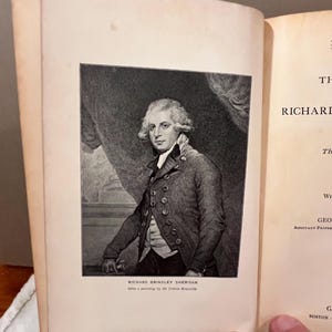 May include: An open book featuring a black and white portrait of Richard Brinsley Sheridan. The portrait is a detailed engraving, with the text "RICHARD BRINSLEY SHERIDAN" and "After a painting by Sir Joshua Reynolds" below the image.