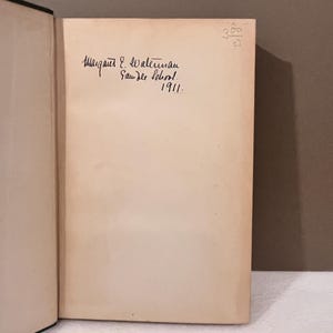 May include: Open book with a cream-colored page featuring handwritten text. The text reads "Margaret E. Waterman, Saunder School, 1911." A small handwritten number is in the upper right corner.