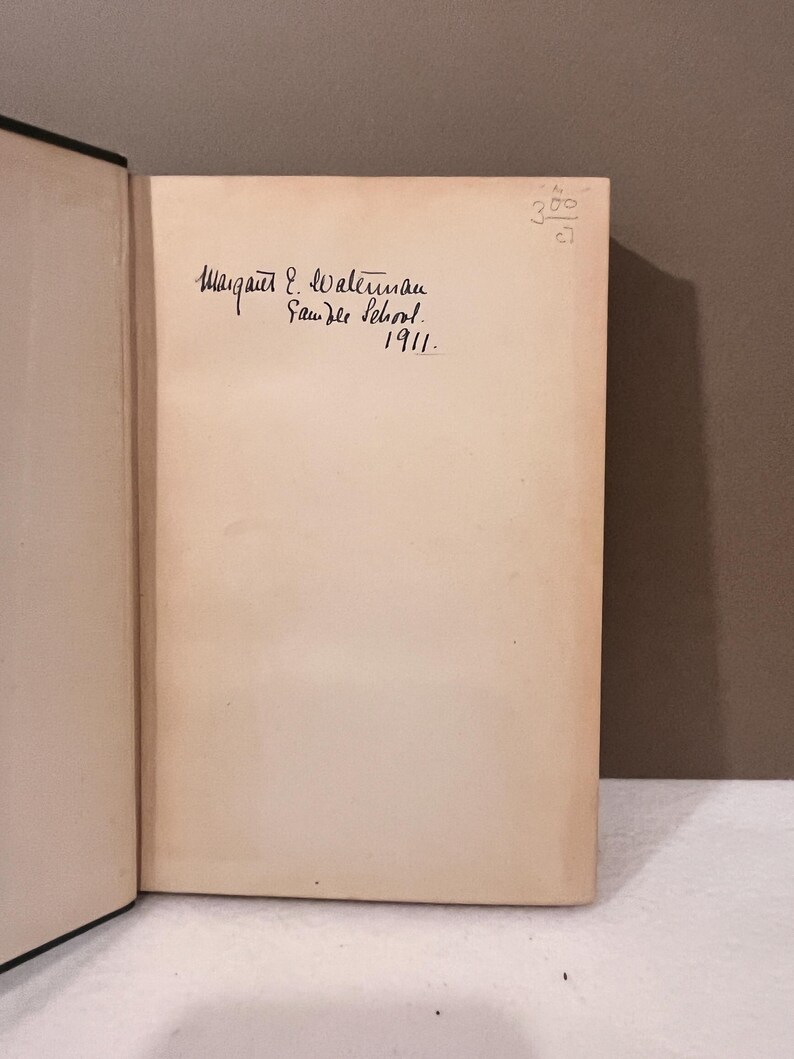 May include: Open book with a cream-colored page featuring handwritten text. The text reads "Margaret E. Waterman, Saunder School, 1911." A small handwritten number is in the upper right corner.