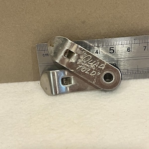 May include: A silver metal Quad Fold bottle opener. The opener is approximately 4 inches long and has the words "Quad Fold" etched on the surface. The opener is lying on a white surface next to a ruler.