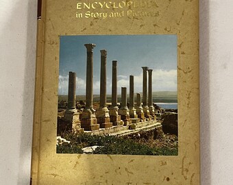 May include: A vintage book titled "The Living Bible Encyclopedia in Story and Pictures." The cover is a light tan with gold lettering and a color image of ancient columns. The words "Art Treasure Edition" are printed at the bottom.