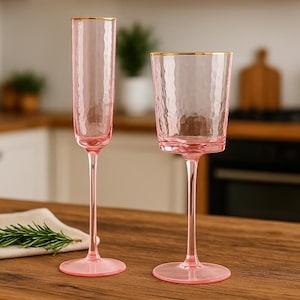 Peut inclure: Deux flûtes à champagne roses et un gobelet à bords dorés. Les verres ont une surface texturée. La verrerie est posée sur une surface en bois.