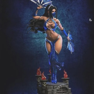 Puede incluir: Figura detallada de un personaje femenino con un atuendo azul, sosteniendo dos abanicos azules. La figura tiene cabello largo y negro y una máscara facial. La base presenta una estructura de piedra con pequeñas llamas.